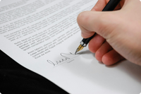Mano firmando un documento legal con bolígrafo dorado sobre fondo blanco y negro